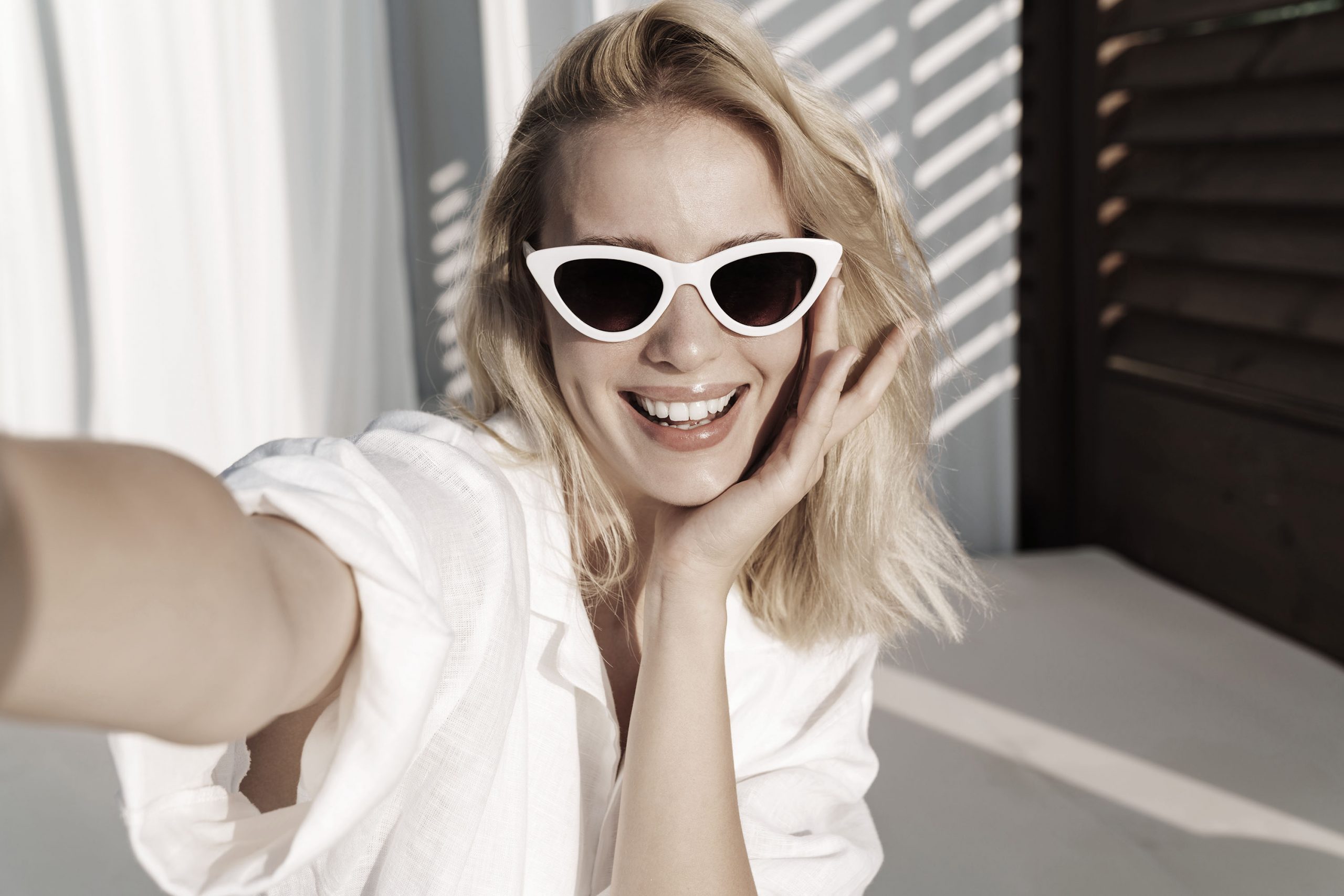 Frau lächelt mit großer Sonnenbrille in die Kamera