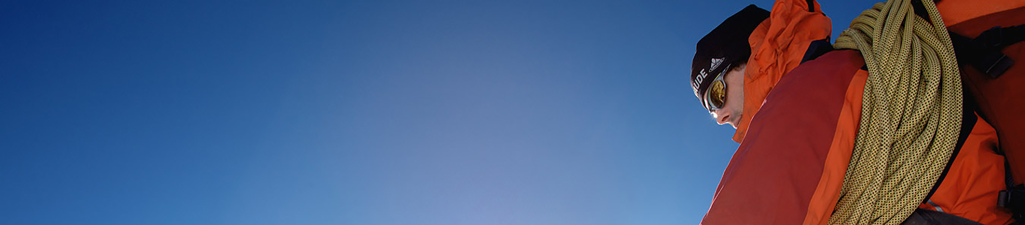 Mann mit Sportbrille und Kletterausrüsting vor blauem Himmel